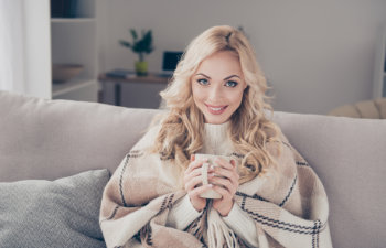 woman sitting on divan wrapped in warm cover light white interior room